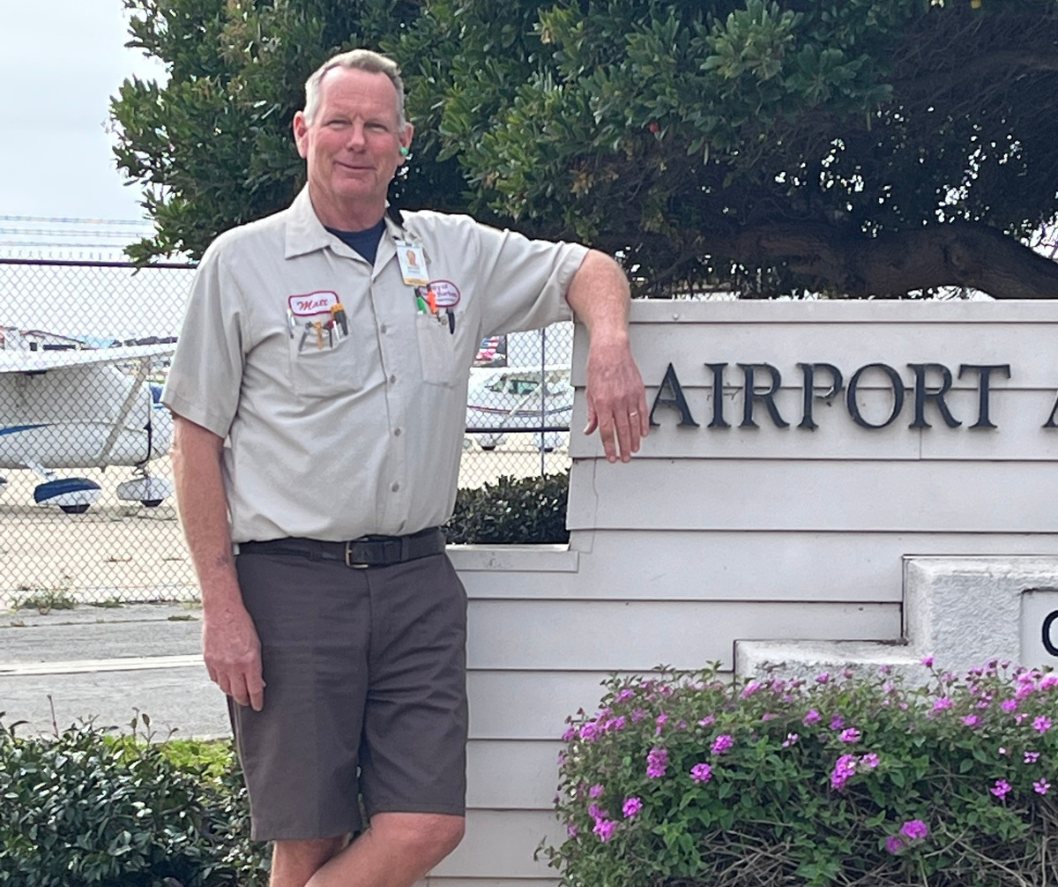 Employee of the Month Matt Donahue standing in front of airport sign