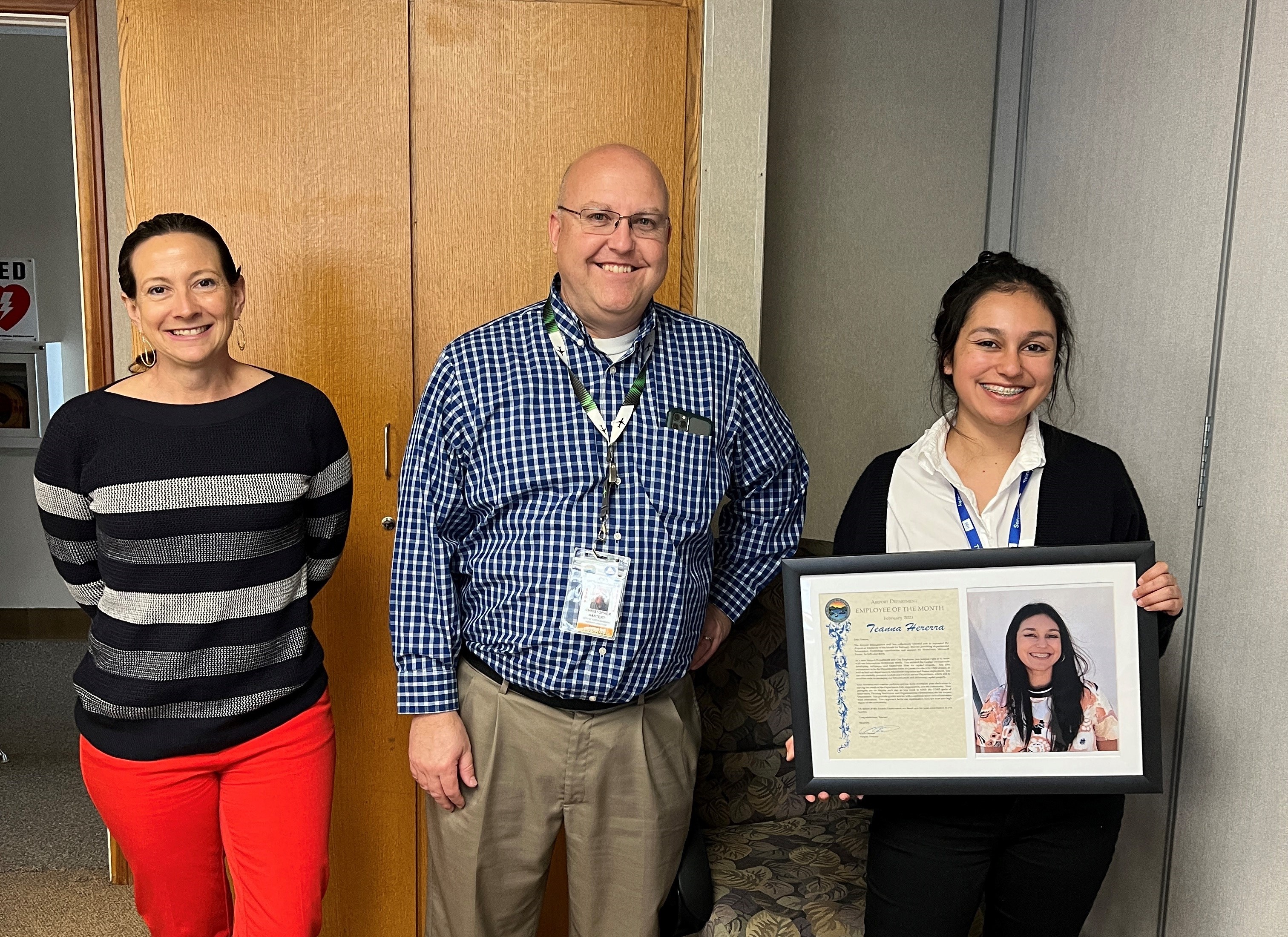 Teanna Herrera holding her recognition plaque, standing next to Chris (Airport Director) and Sara (Development Manager)