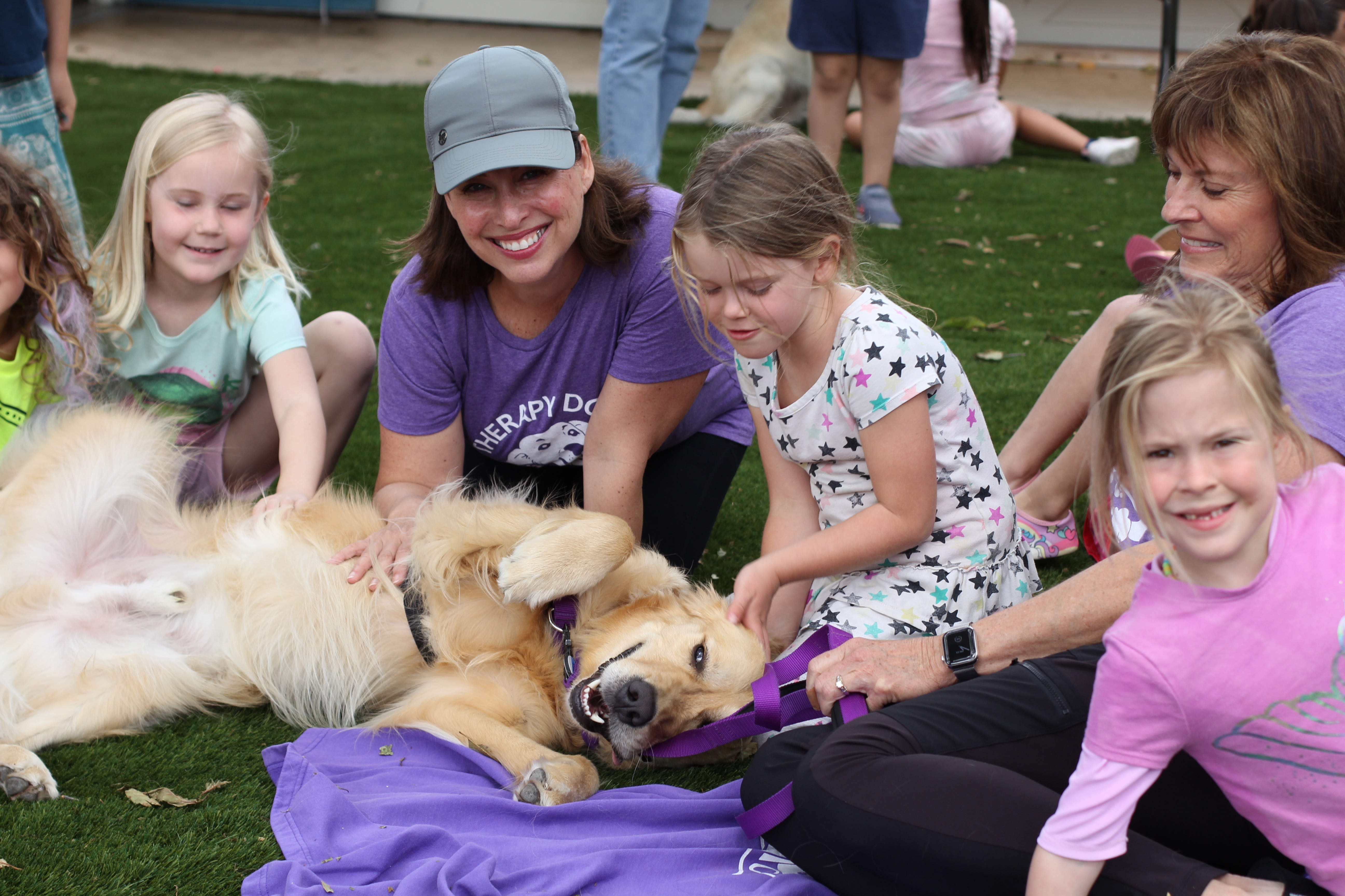 Therapy dog laying in grass with kids