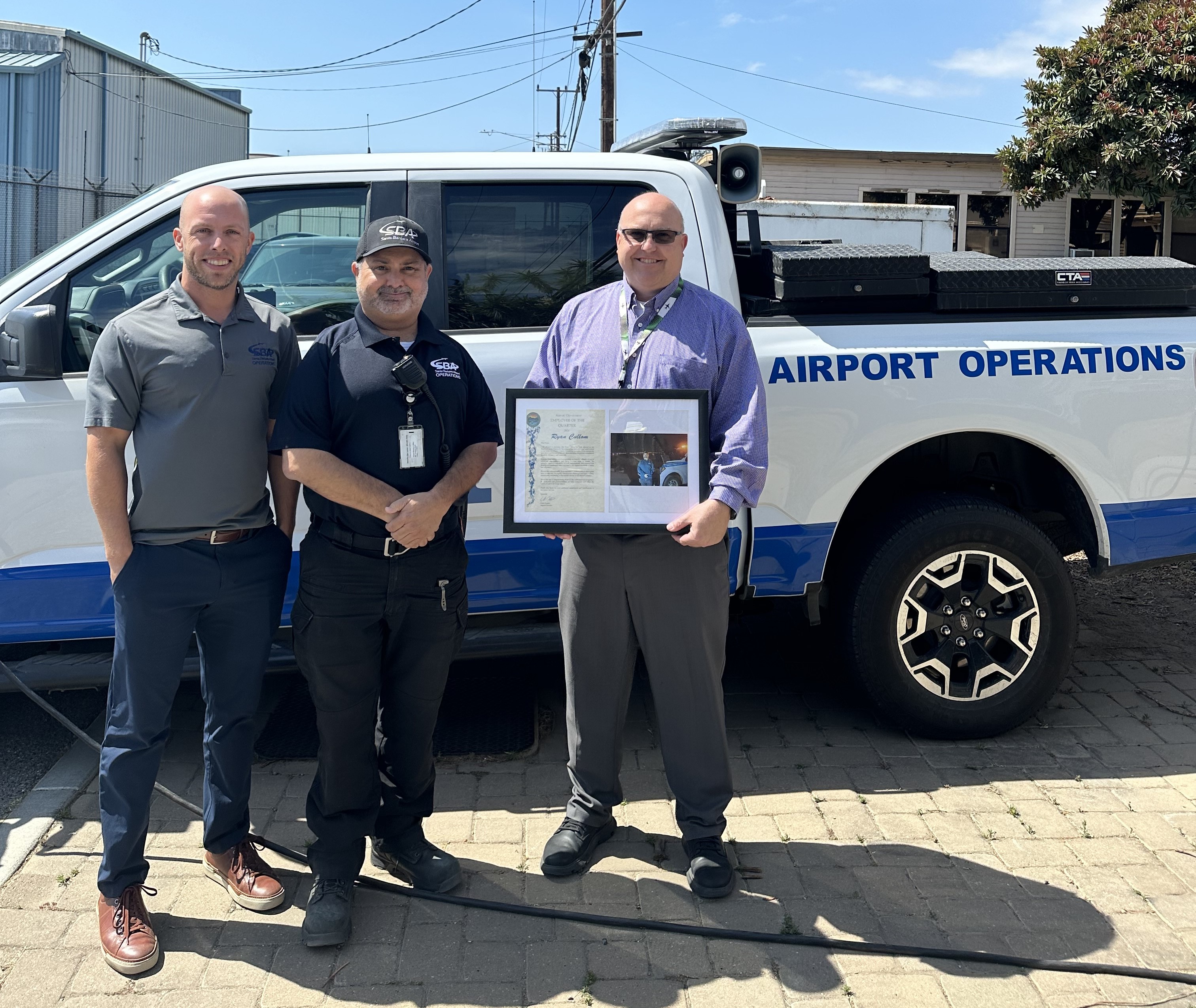 Ryan Cullom poses with two airport staff holding an award plaque.