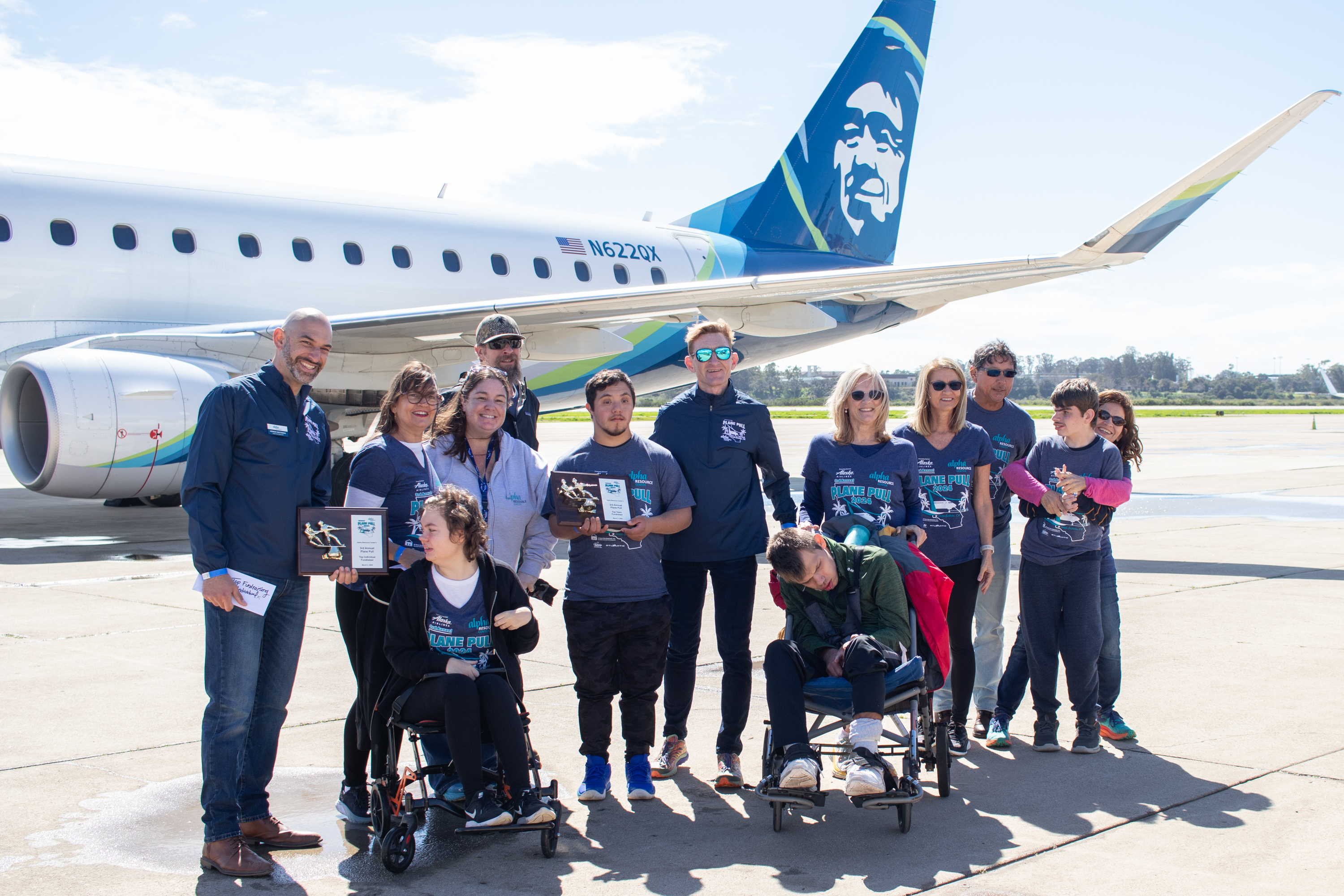 A group of people pose in front of an Alaska Airlines plane.