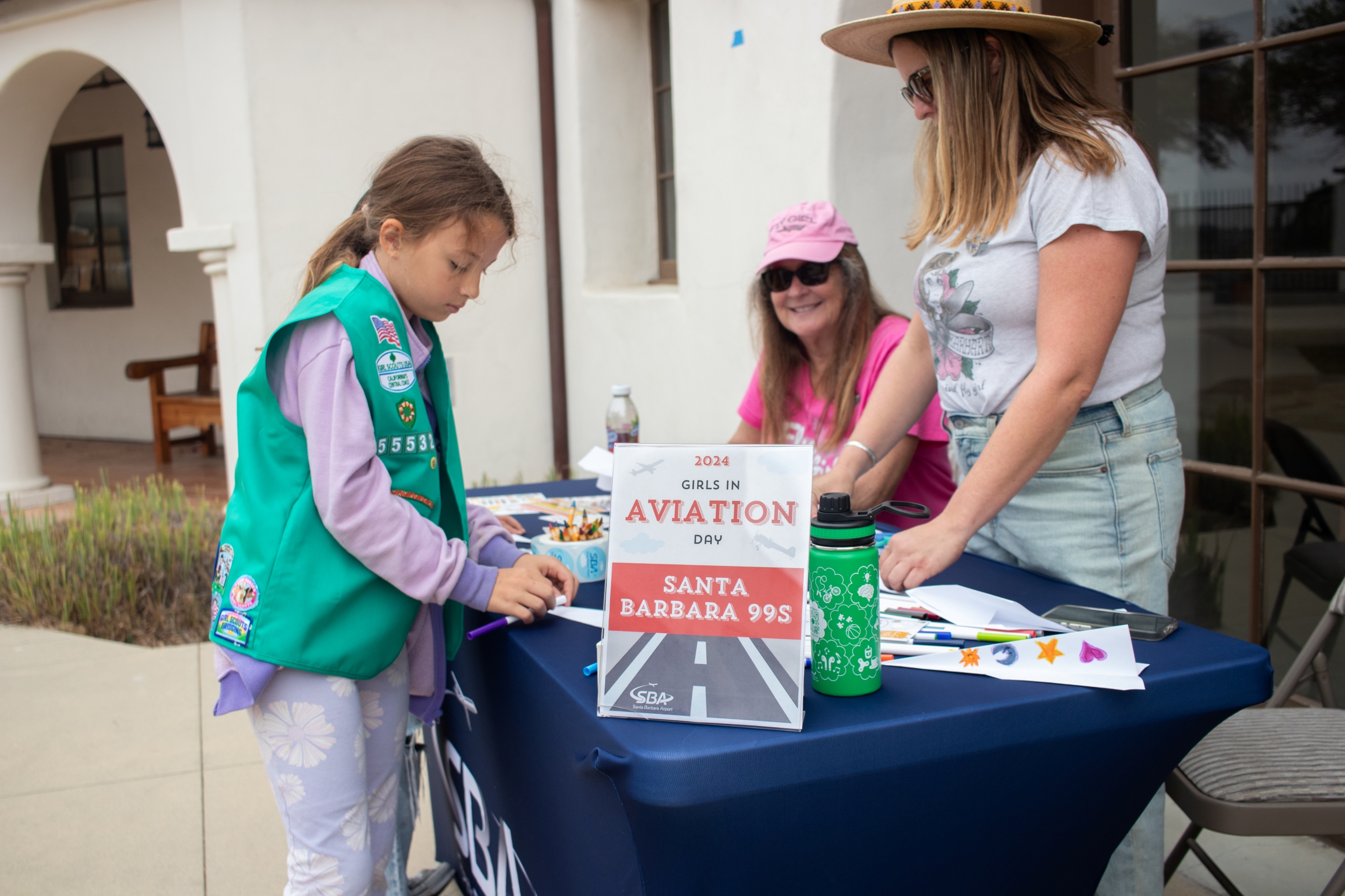 A girl scout talks to two female pilots at a table.