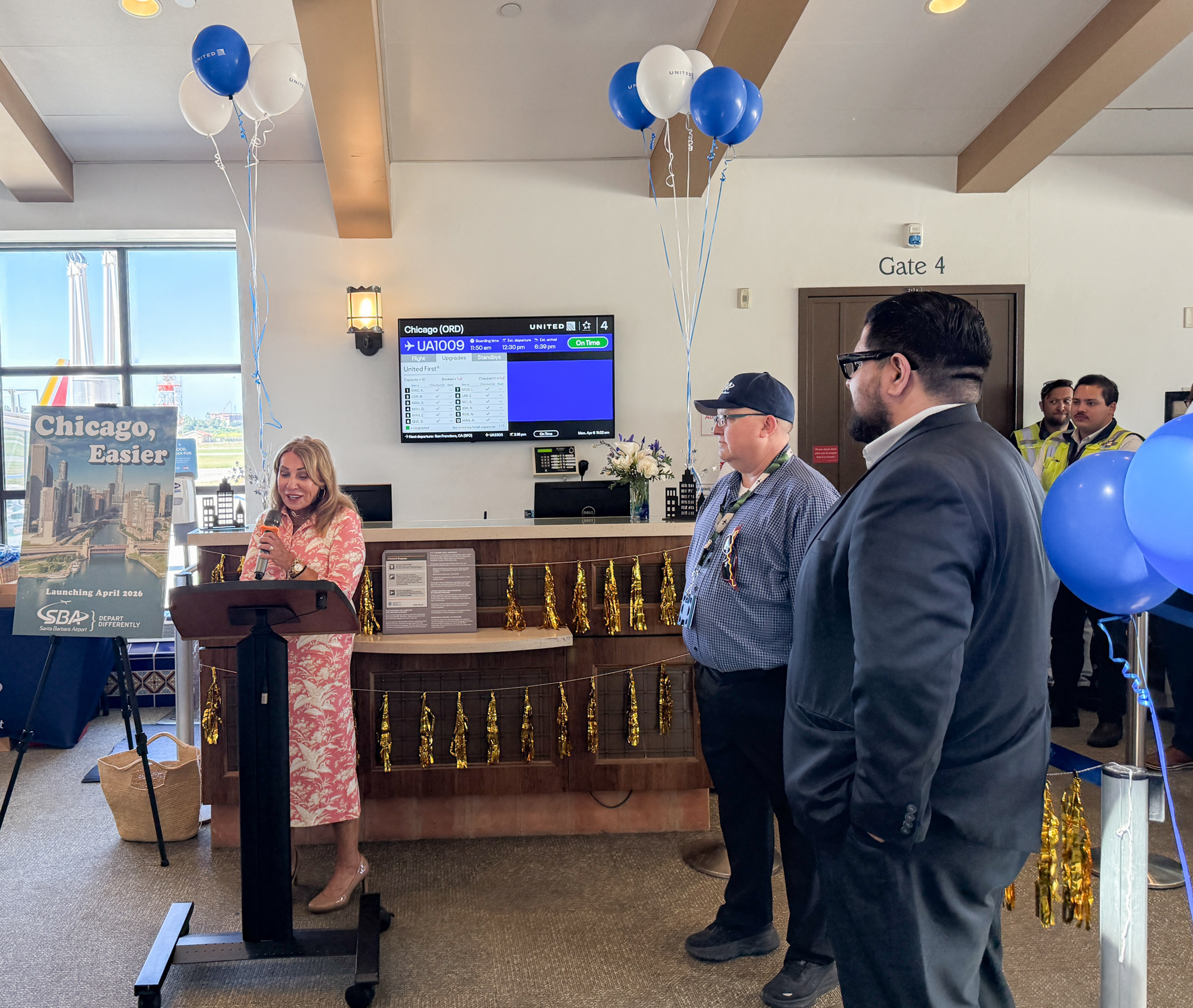 Kathy Janega-Dykes (Visit Santa Barbara) and Chris Hastert (Santa Barbara Airport Director) speak at a podium to welcome the passengers.