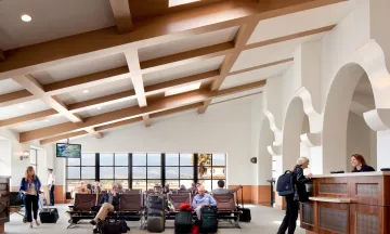 People waiting at an airport terminal and a women talking to a clerk