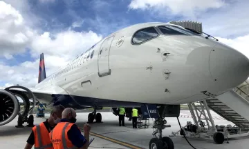 Delta A220-300 parked at a gate with two airline employees standing next to it
