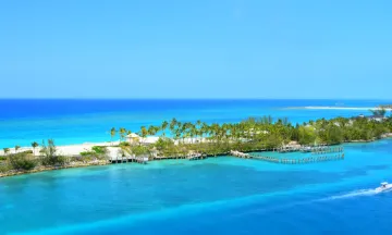 An aerial shot of an island in the Bahamas with crystal blue water and palm trees.