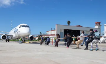 A group of people pull an airplane by a rope.