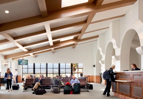 People waiting at an airport terminal and a women talking to a clerk