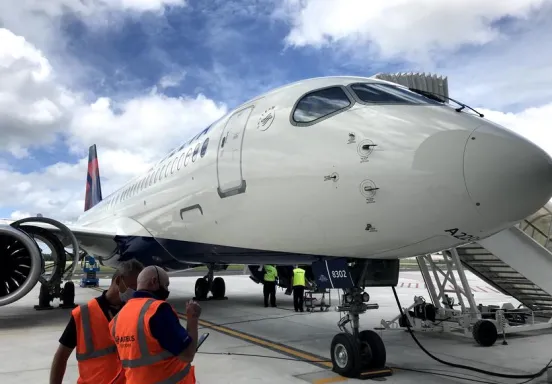 Delta A220-300 parked at a gate with two airline employees standing next to it