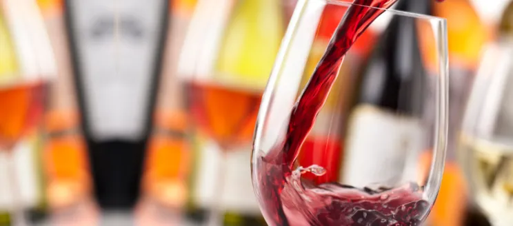 Red wine being poured into a wine glass with wine bottles in the background