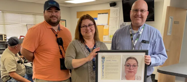 Julia poses with two airport staff and her Employee of the Month plaque