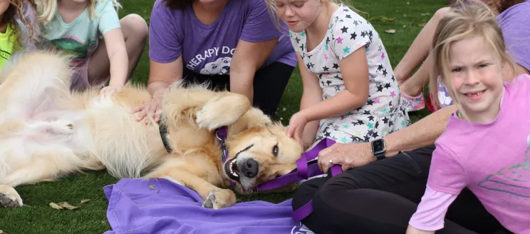 Therapy dog laying in grass with kids