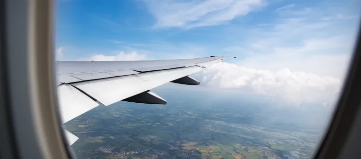 An airplane window overlooking the wingtip and ground below 