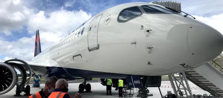 Delta A220-300 parked at a gate with two airline employees standing next to it