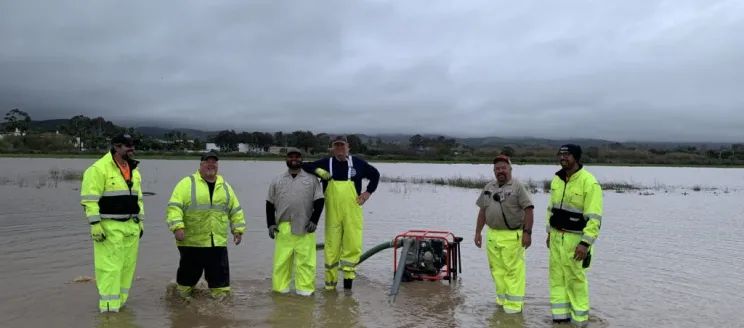 Maintenance workers smiling knee deep in water on flooded airfield