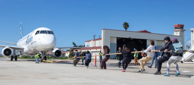 A group of people pull an airplane by a rope.