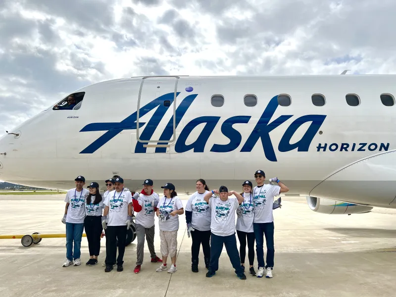 Team of 10 poses in front of Alaska Airlines plane