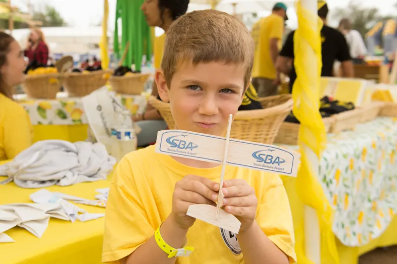 Child poses with a small bamboo glider in front of SBA's booth at Lemon Festival